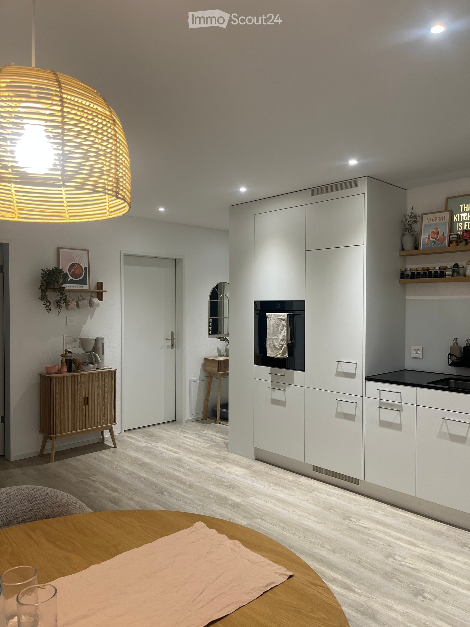Modern kitchen with white cabinets, a round wooden dining table, a coffee maker, and a large hanging light fixture.