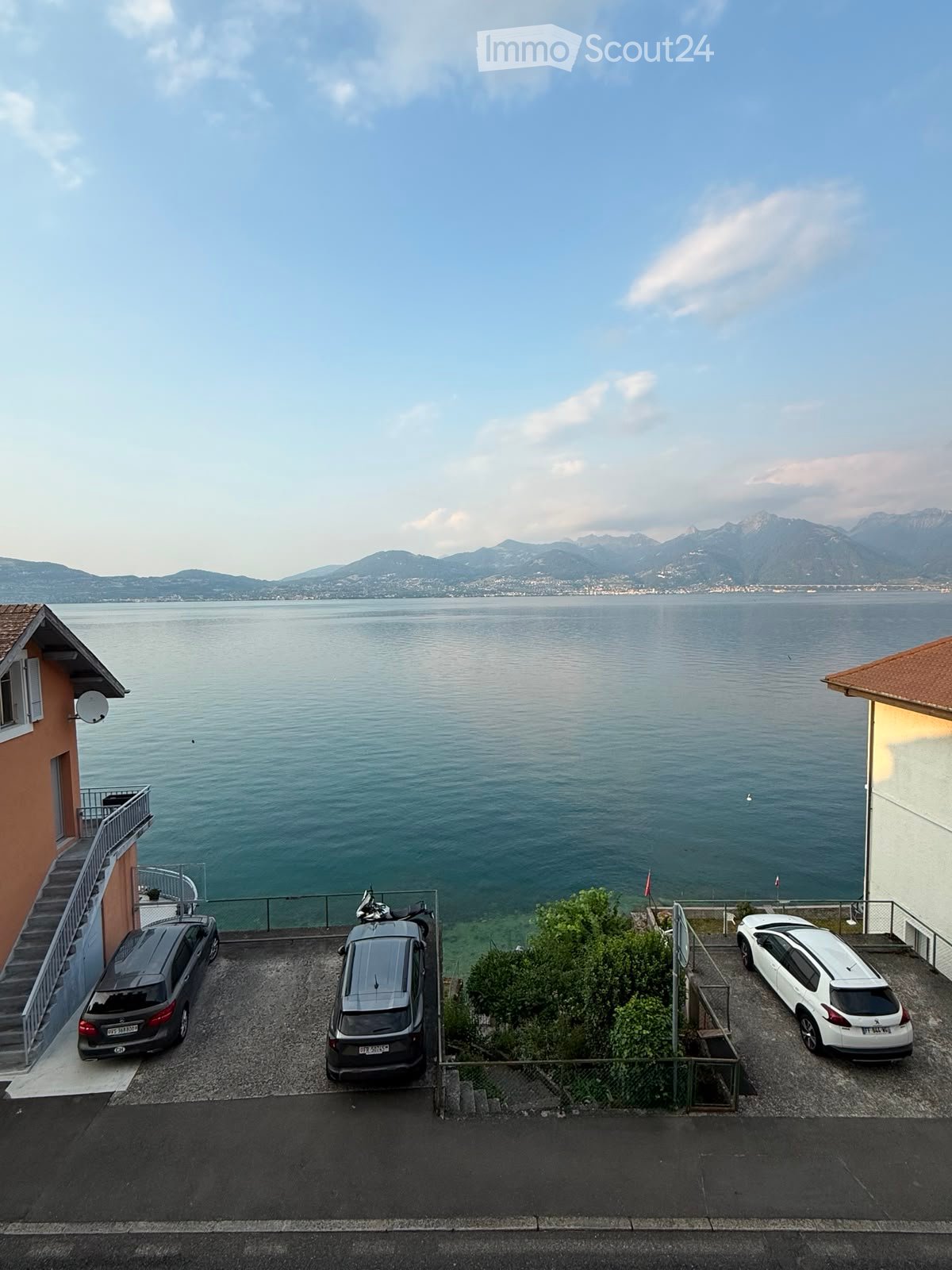 Parking area with three cars, overlooking a large body of water with distant mountains.