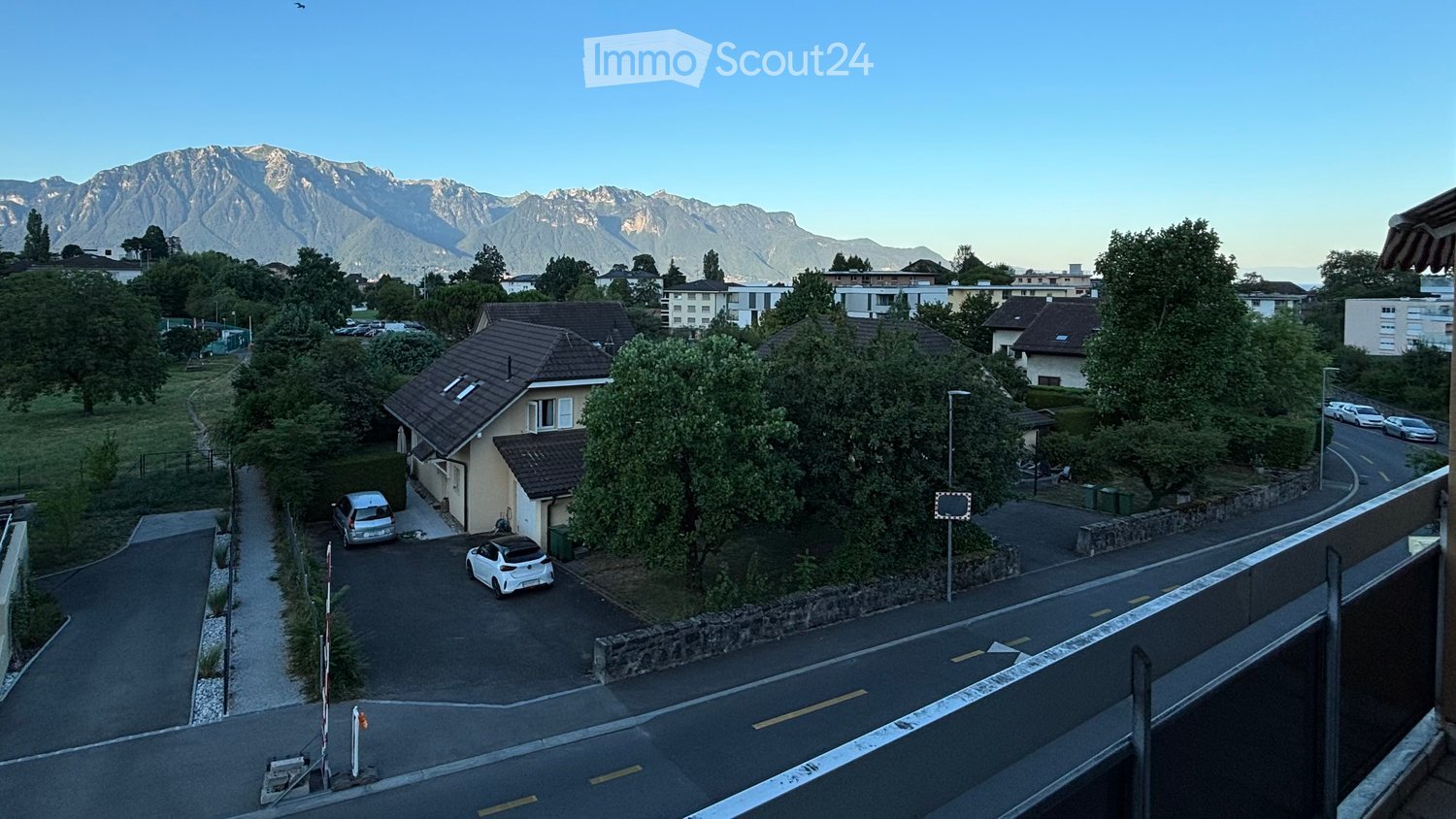 Aerial view of a residential area with houses, parked cars, and a scenic mountain backdrop.