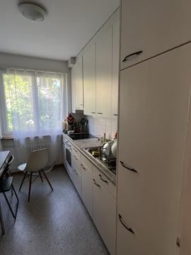Modern kitchen with white cabinets, a sink, an oven, and a small dining area with a chair and table.