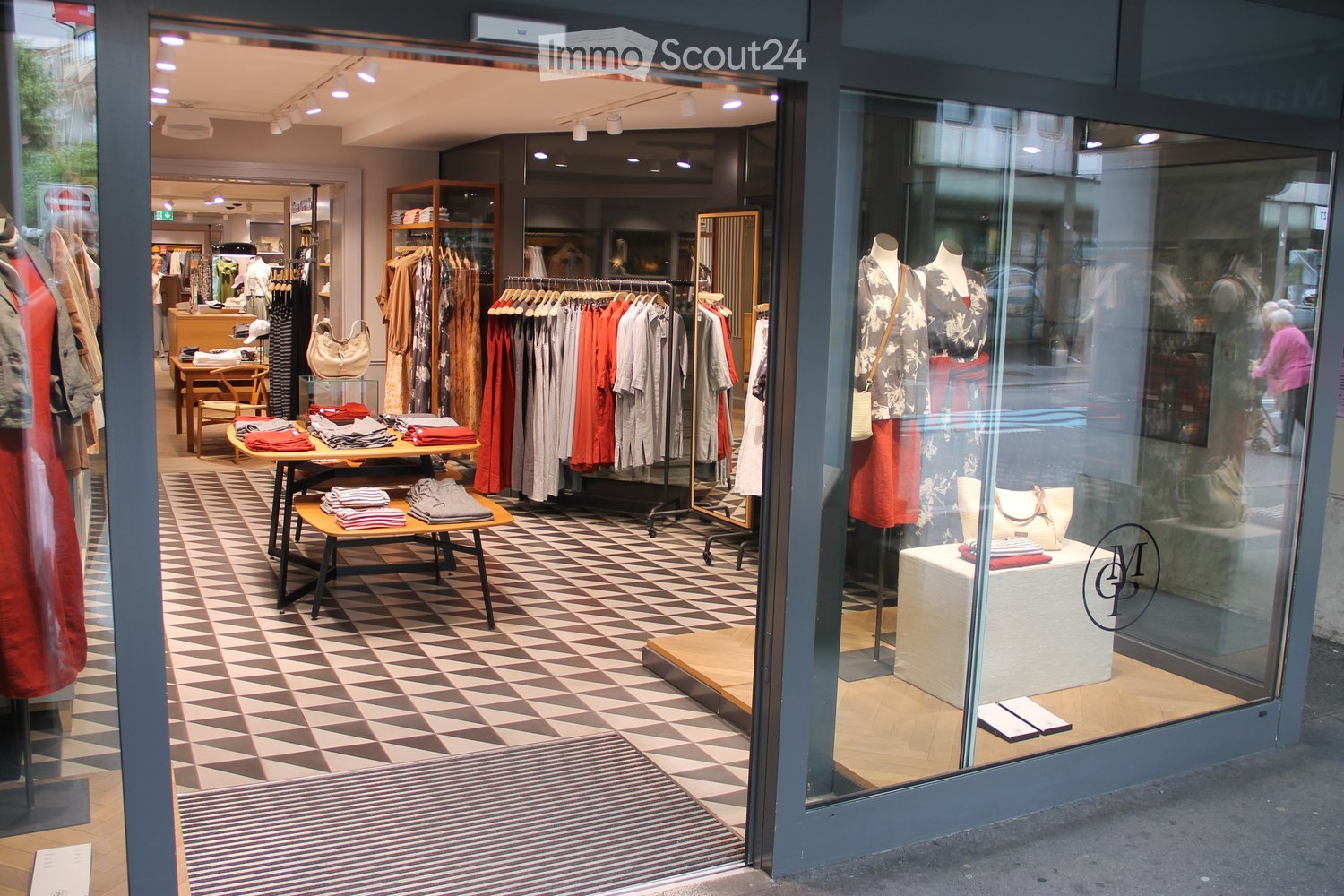 Fashion boutique interior with checkered flooring, clothing racks, mannequins, and display tables.