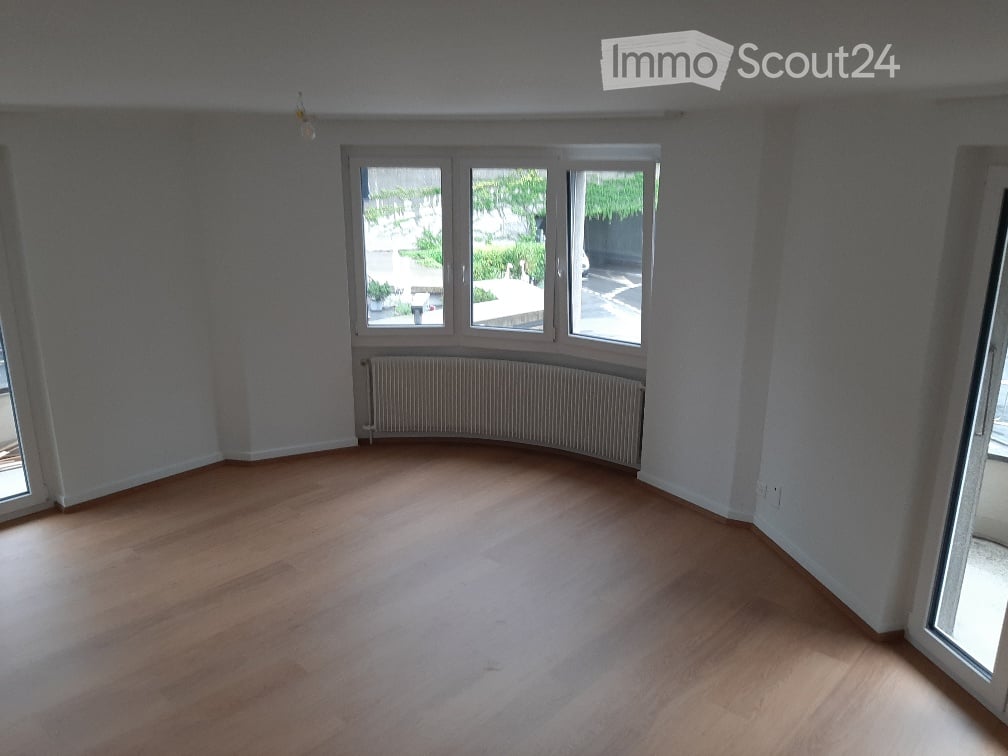 Empty room with wooden flooring, white walls, large windows, and a radiator. No furniture or equipment present.