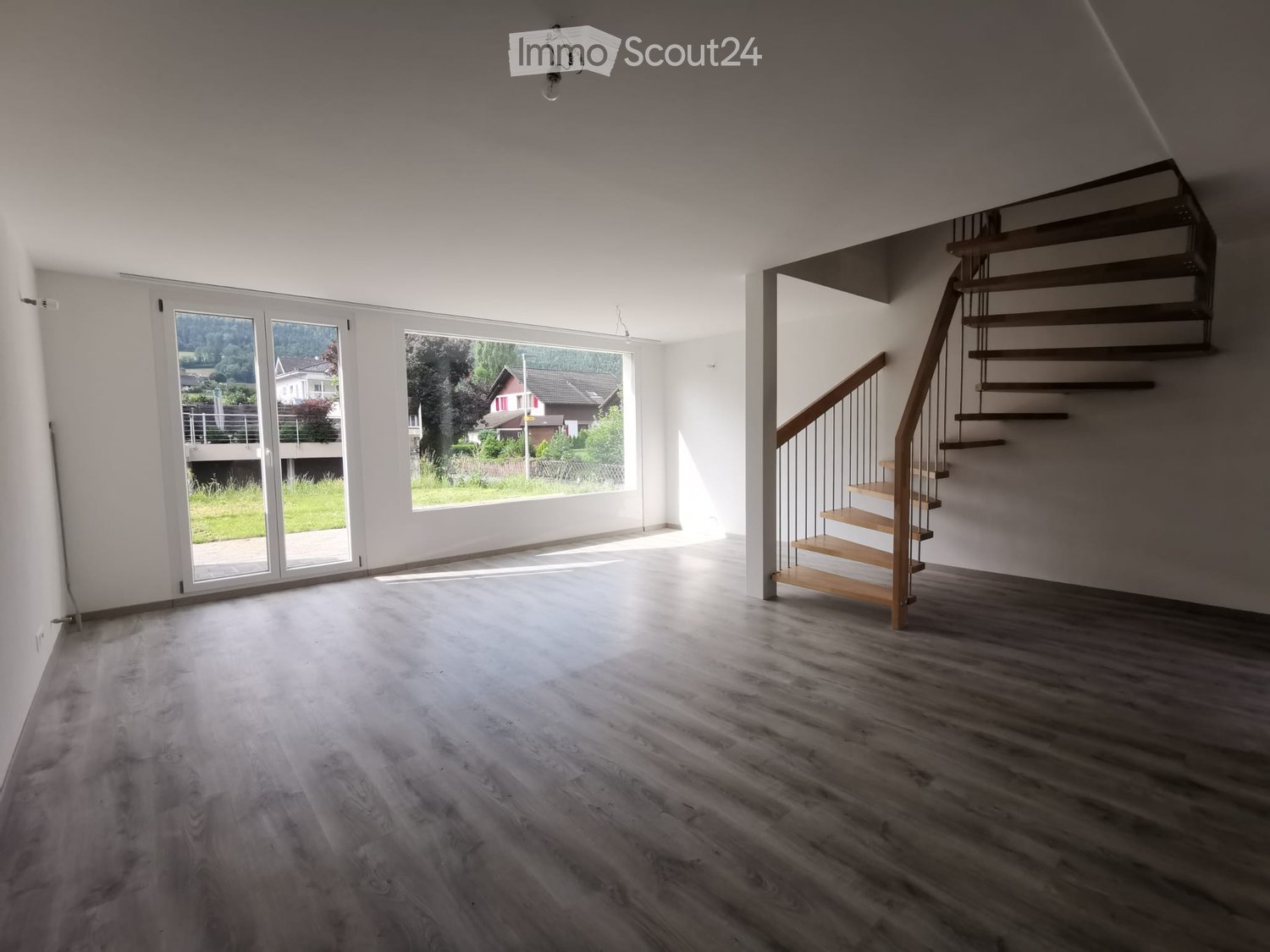 Empty room with wooden flooring, large windows, and a staircase leading to an upper level.