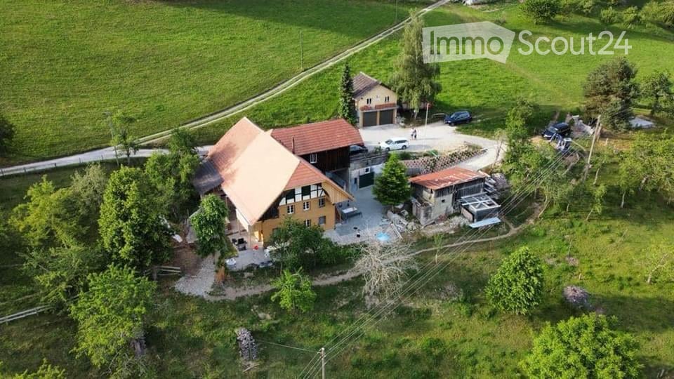 Aerial view of a two-story house with a garage, surrounded by greenery and a parking area.