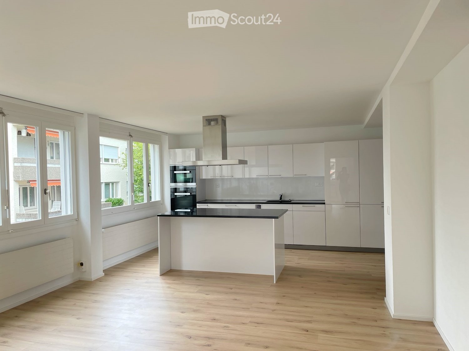 Modern kitchen with white cabinets, stainless steel appliances, a central island, and large windows offering a view of the street.