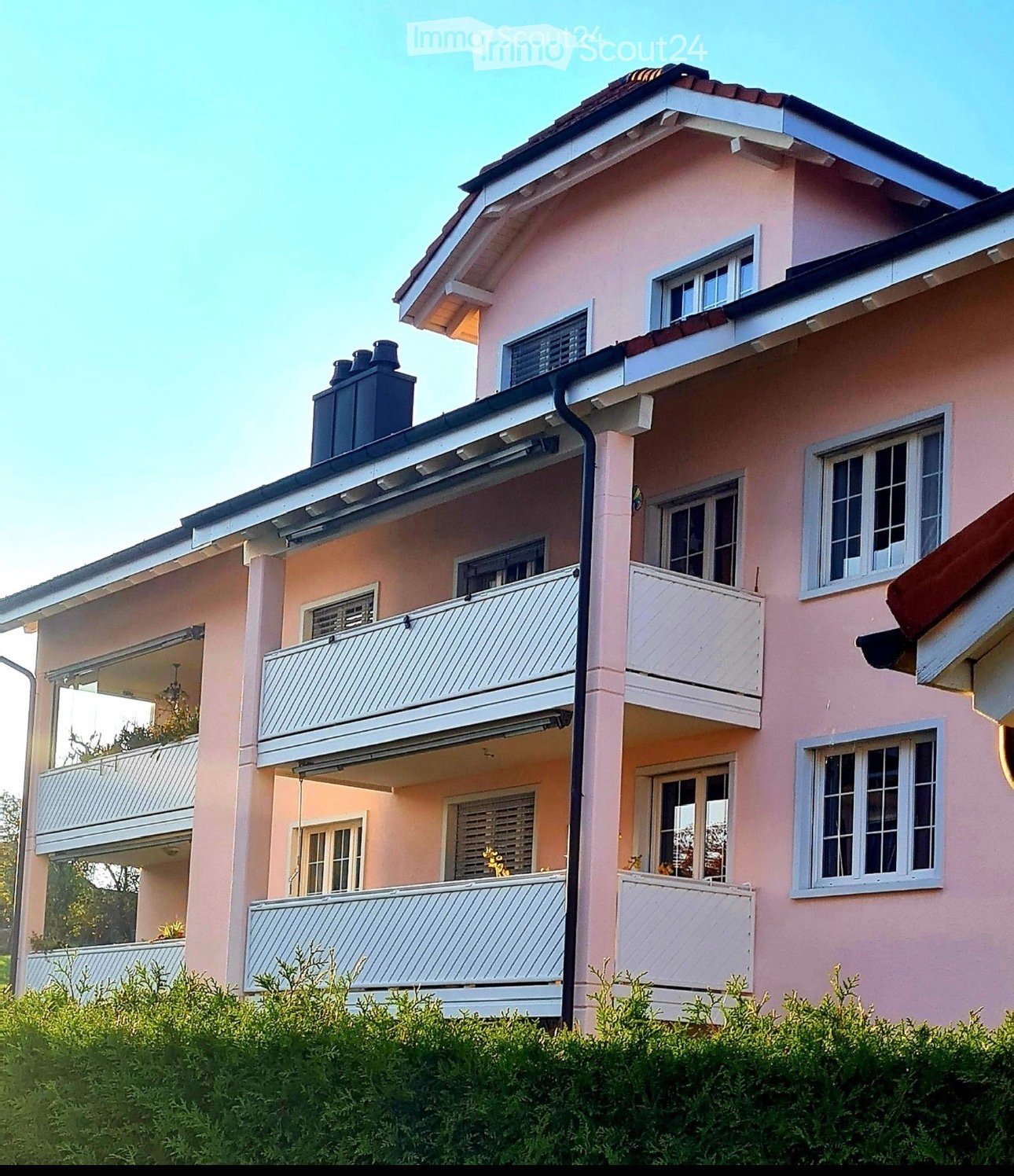 Two-story pink house with white-framed windows, multiple balconies, and a chimney on the roof.