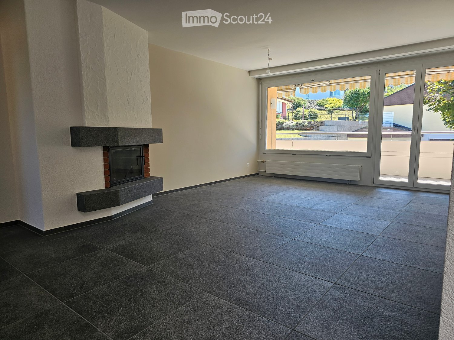 Empty room with dark tiled flooring, a built-in fireplace, large sliding glass doors leading to an outdoor area, and a radiator under the windows.