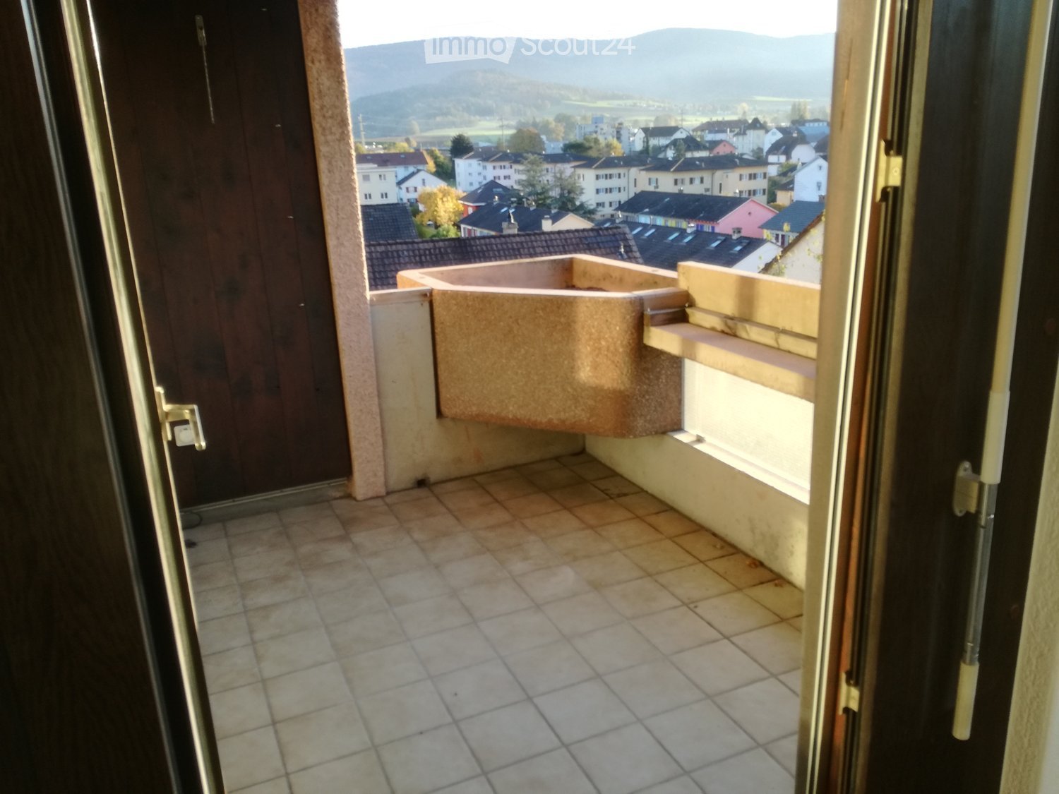 Balcony with tiled floor, small built-in seating area, and view of town and hills.