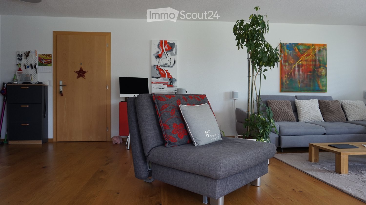 Modern living room with grey sofa, coffee table, screen, plant, cabinet, and artwork.