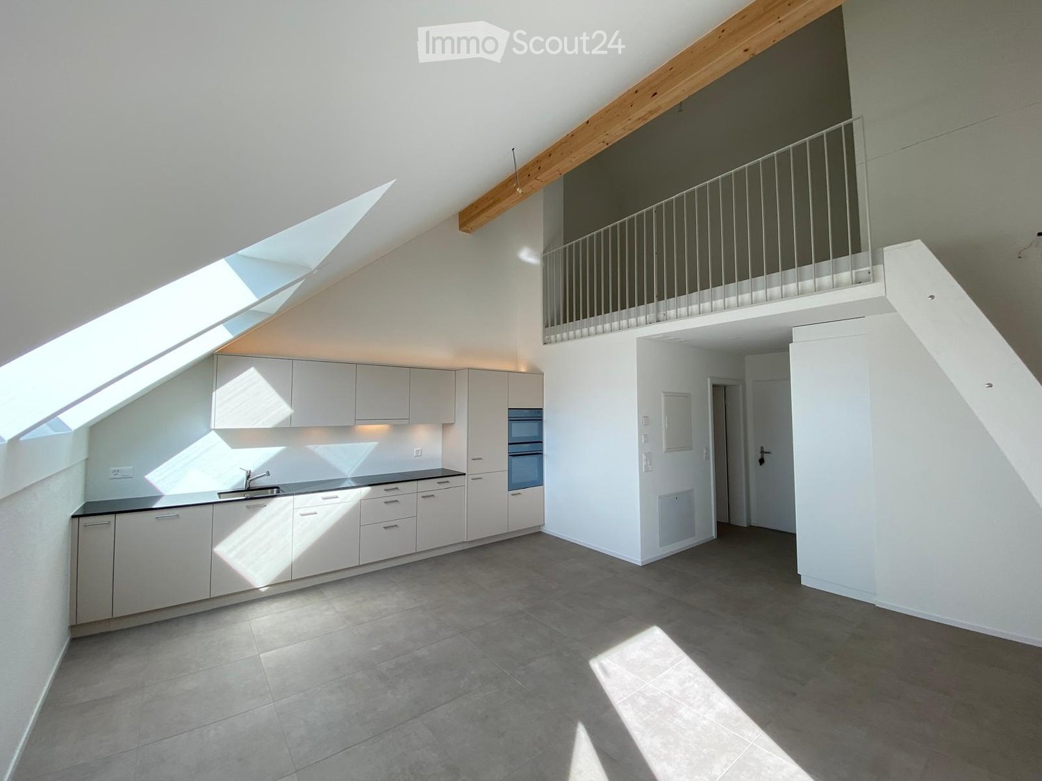 Bright, modern kitchen with white cabinets, stainless steel sink, and built-in oven. The space features large windows and a raised ceiling with wooden beams.