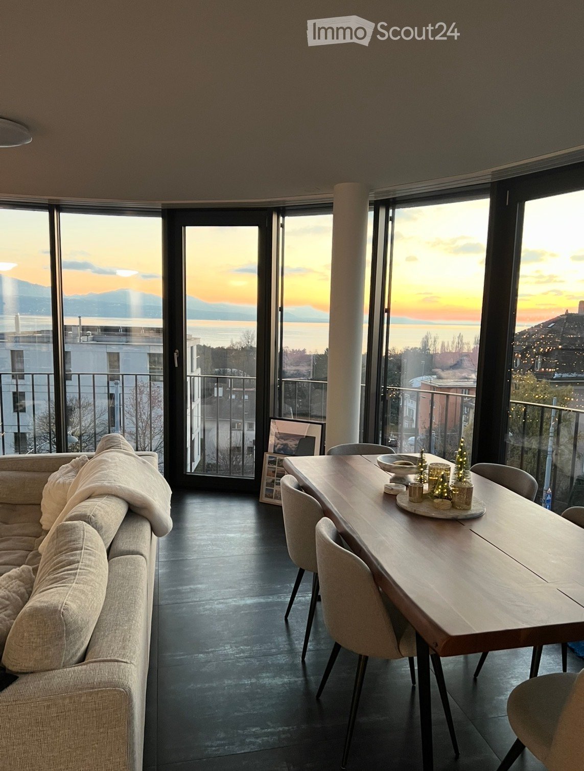 Modern living and dining area with large windows offering a scenic view, featuring a sofa, dining table, and decorative candles.
