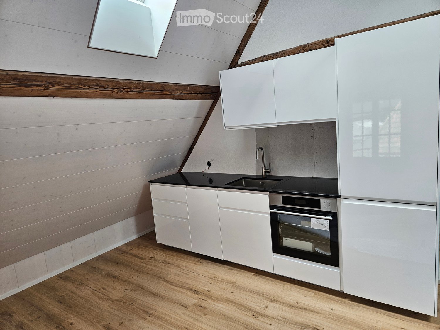 Modern kitchen with white cabinets, black countertop, wooden floor, and built-in oven.