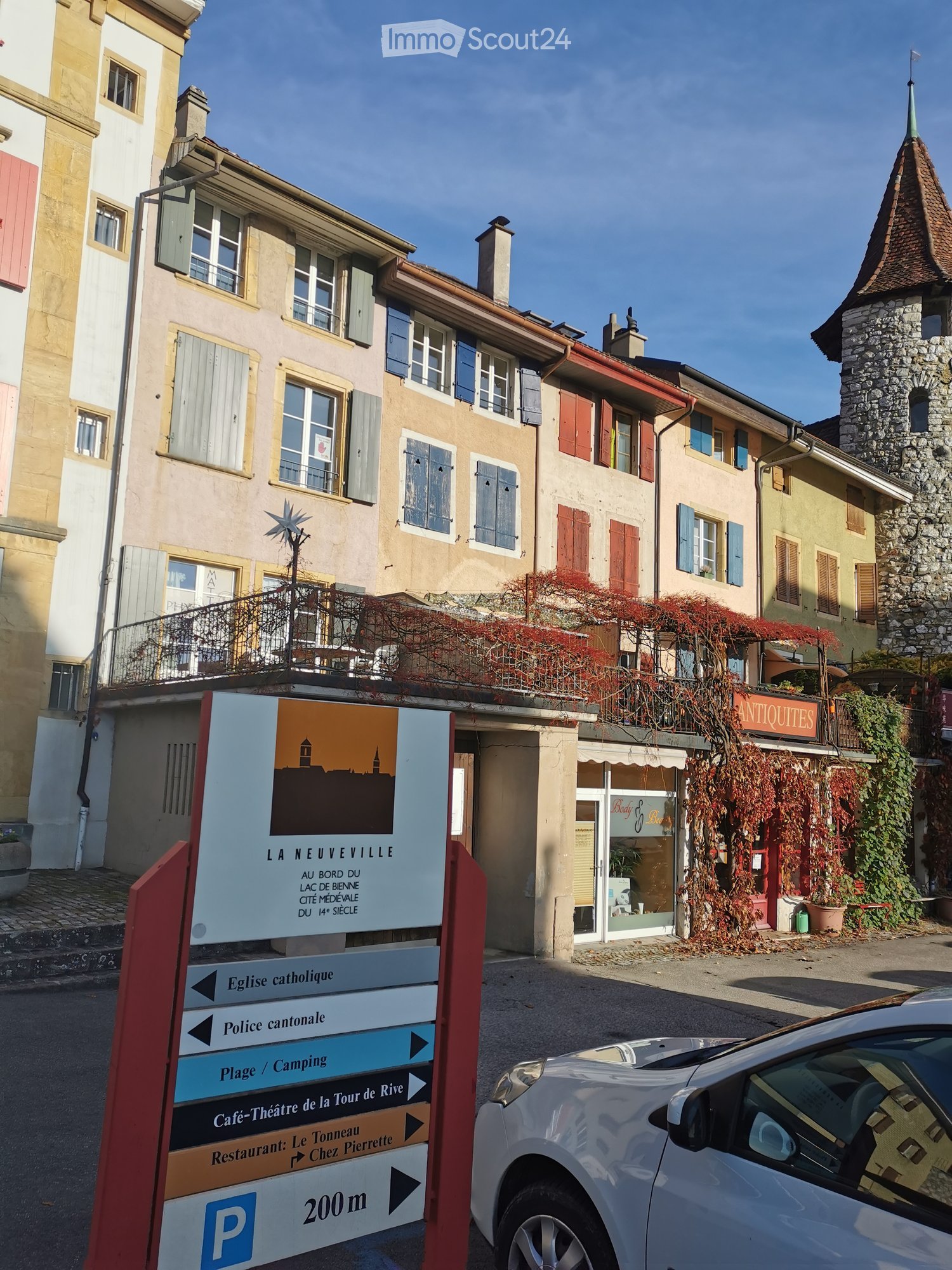 An image of a building with lots of windows, a tower, a sign and a car parked in front