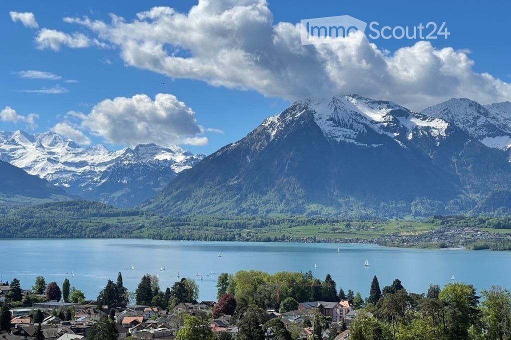 Panoramic view of a serene lake surrounded by snow-capped mountains, with a small town visible along the shoreline.