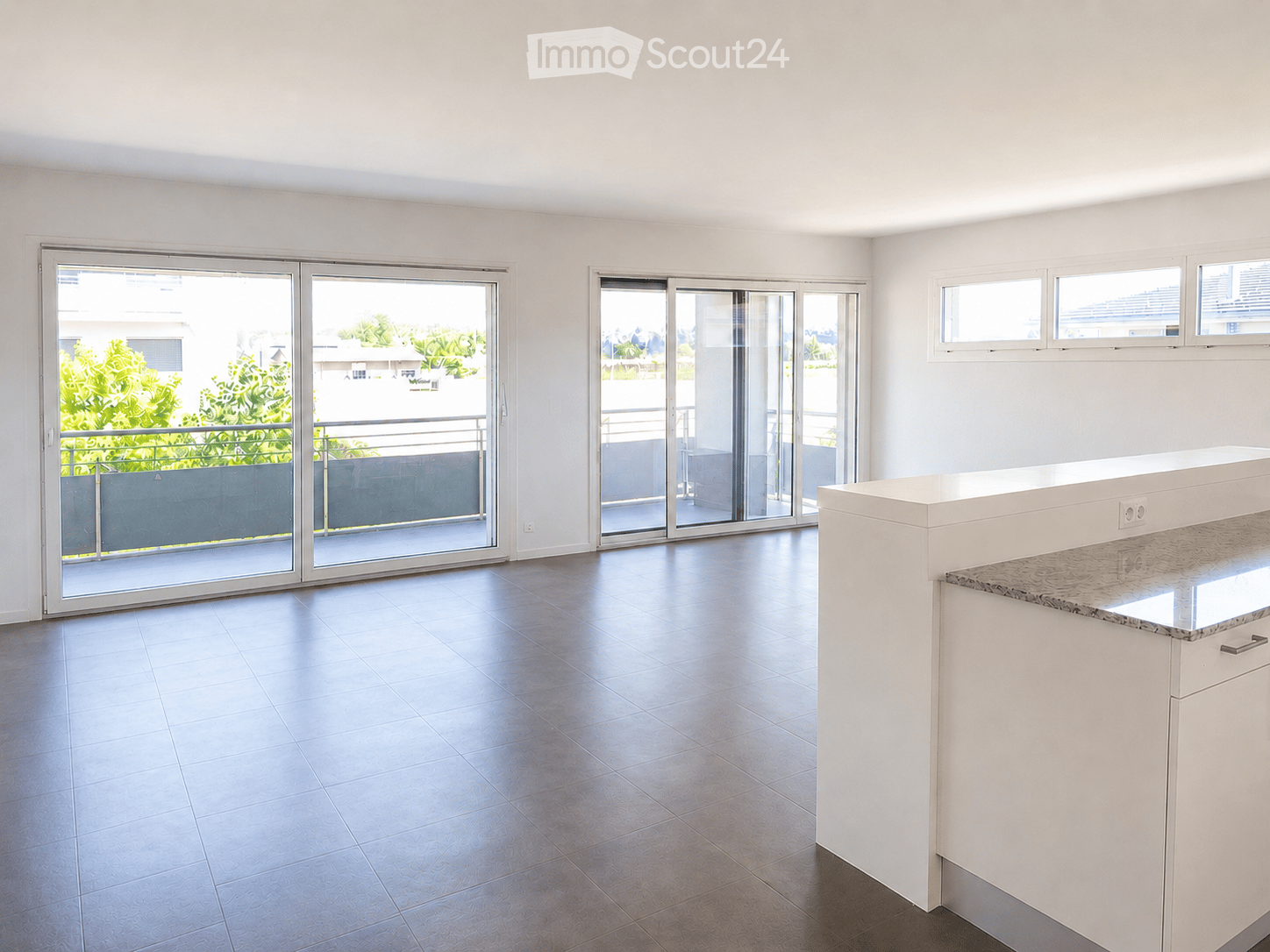 Empty room with white walls, tiled floor, and large sliding glass doors leading to a balcony with a view of greenery.