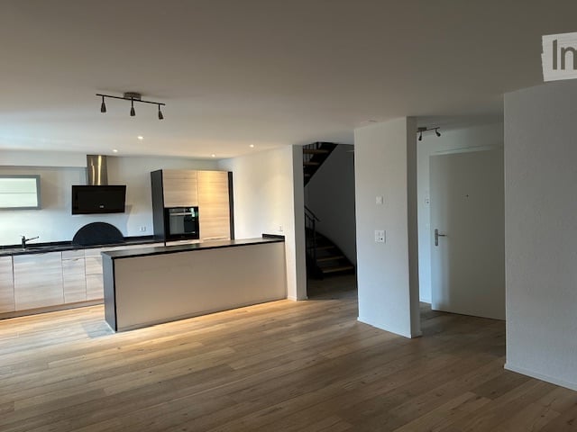 Modern kitchen with light wood flooring, white cabinets, stainless steel appliances, and a central island.