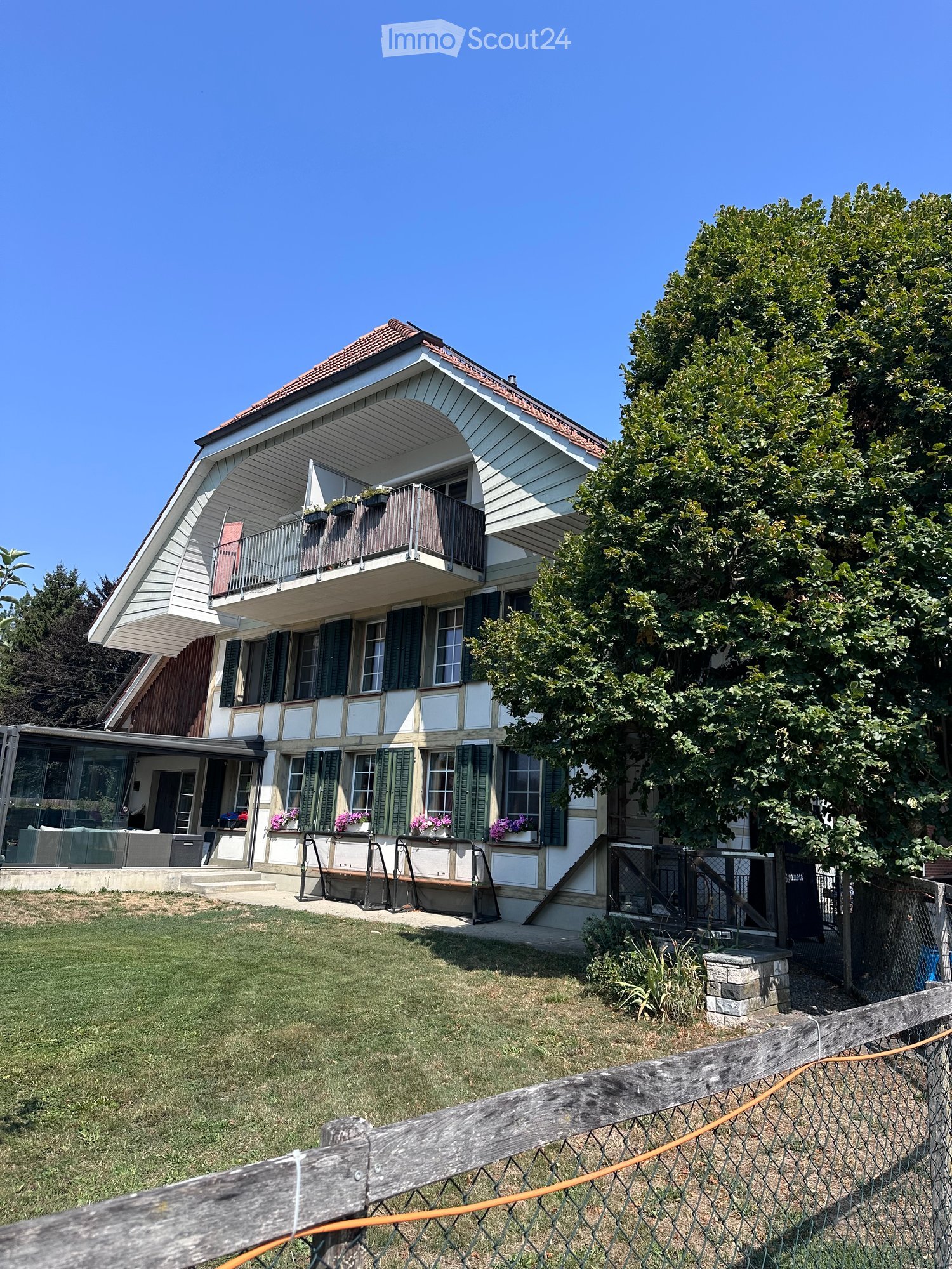 Two-story house with a balcony, green shutters, and flower boxes. The house has a modern design with a mix of white and gray siding and a red-tiled roof.