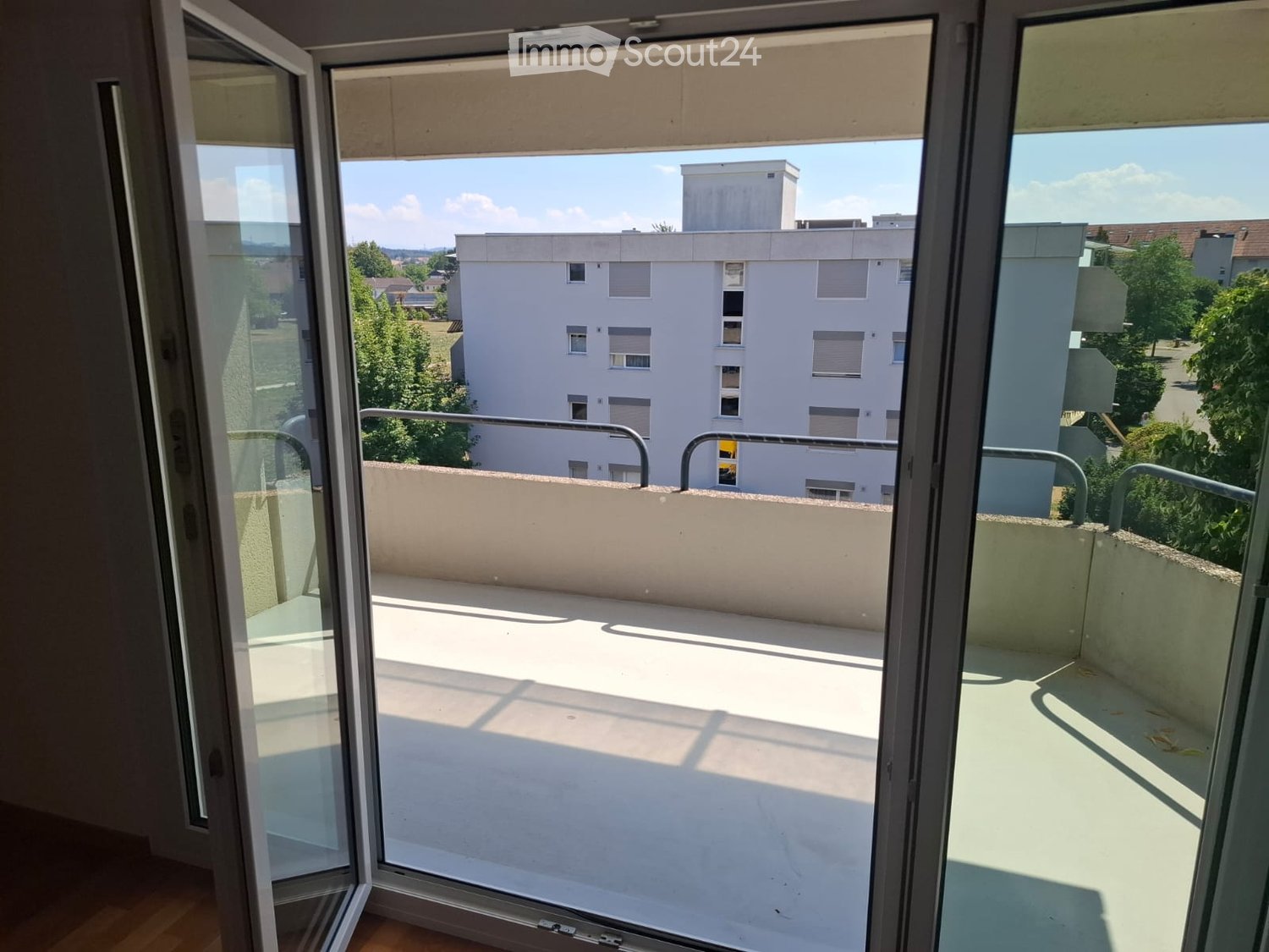 Open balcony with metal railings, overlooking a residential area with buildings and greenery.