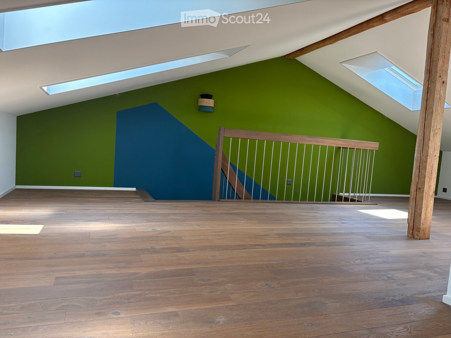 Empty attic space with wooden flooring, green and blue walls, skylights, and a wooden staircase leading to another level.