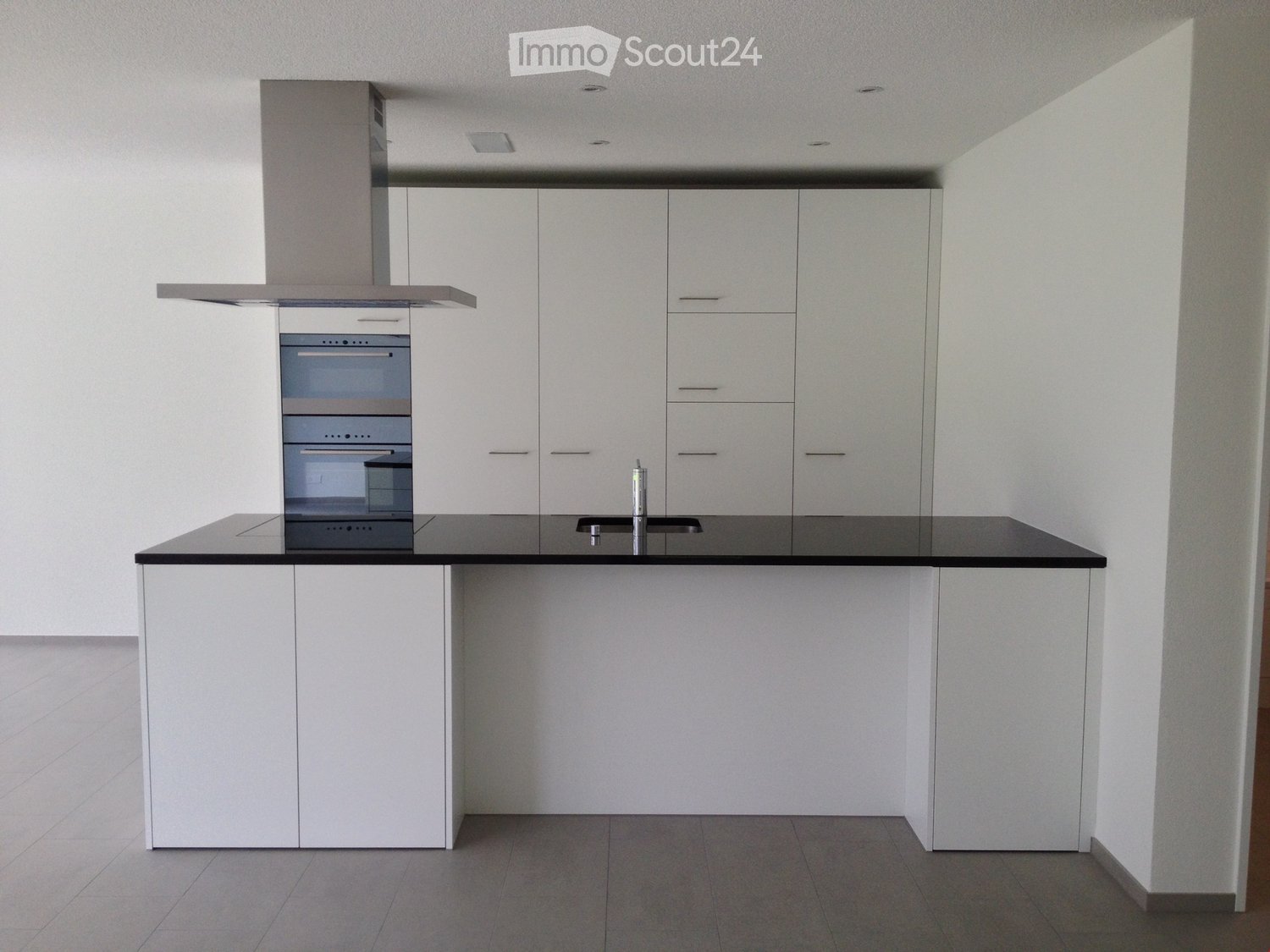 Modern kitchen with white cabinets, black countertop, built-in oven, and a sink with a faucet.