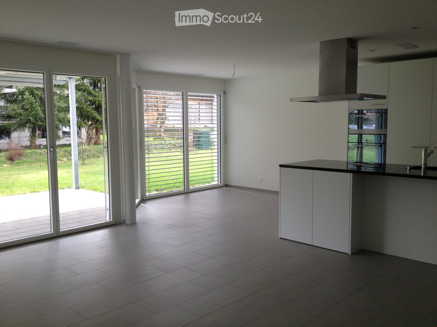 Empty kitchen with white cabinets, a countertop, and large sliding glass doors leading to a patio and garden.