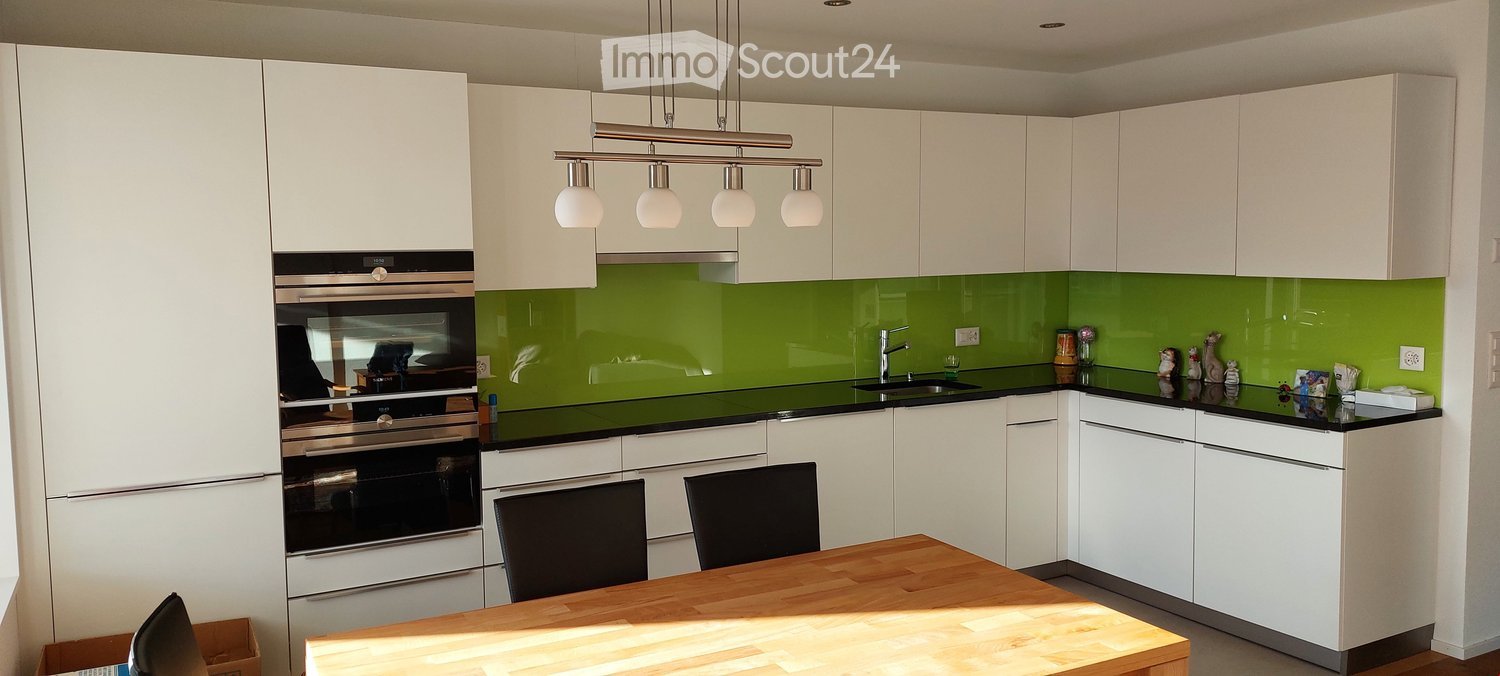 Modern kitchen with white cabinets, green backsplash, black countertop, stainless steel oven, and a wooden dining table with chairs.