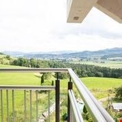 Balcony with metal railing, overlooking a green field and distant mountains.