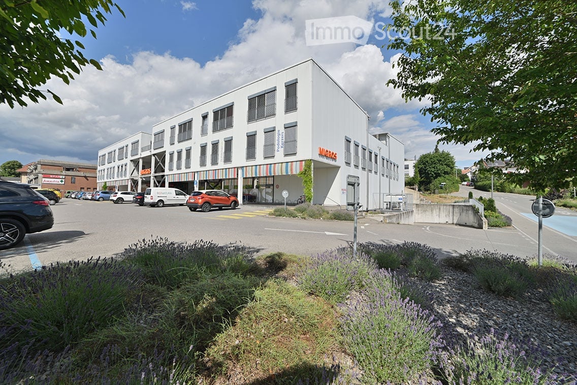Modern multi-story building with white facade and large windows, featuring a colorful striped awning and signage for "Micros".