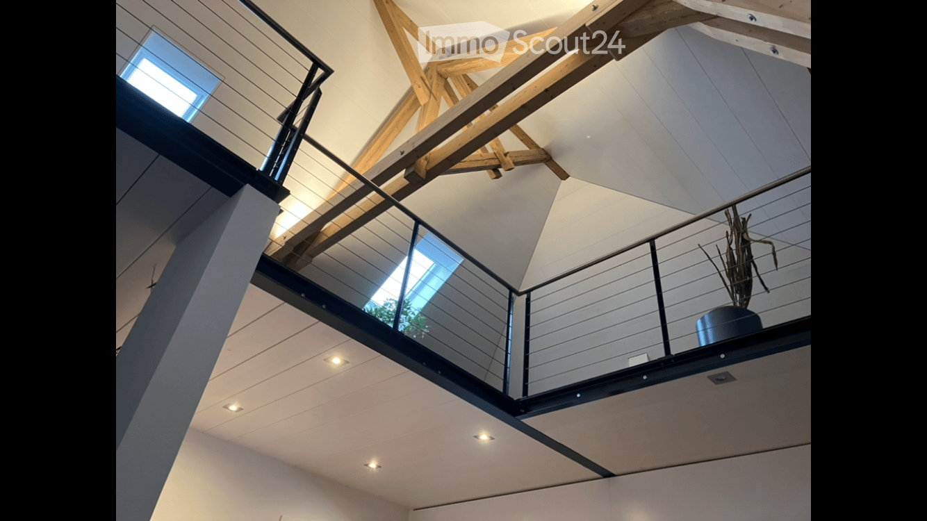 Modern interior with exposed wooden beams, glass railing, and recessed lighting, featuring a plant in a pot on the balcony.