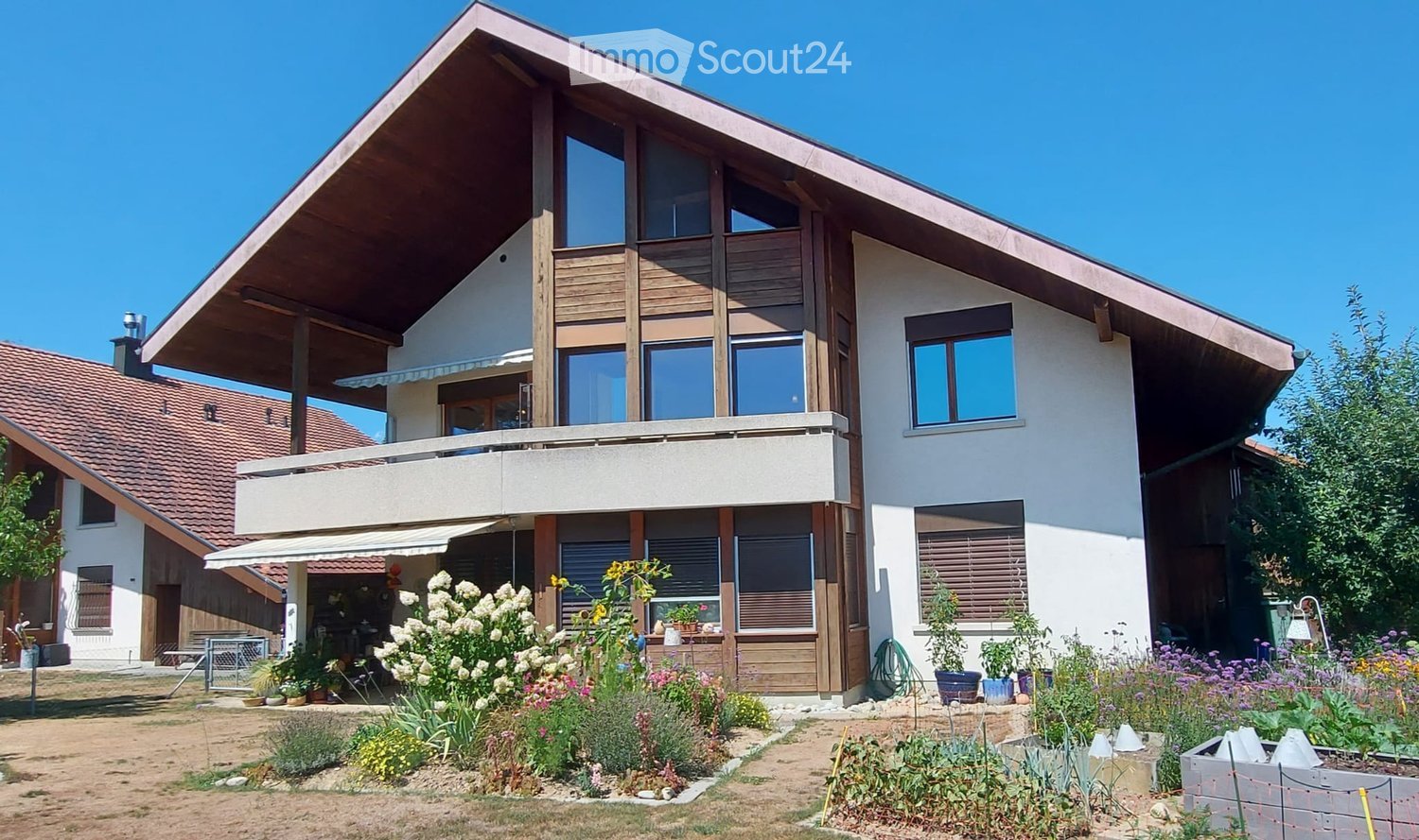 Two-story house with a modern design, featuring large windows, a balcony, and a well-maintained garden with various plants and flowers.