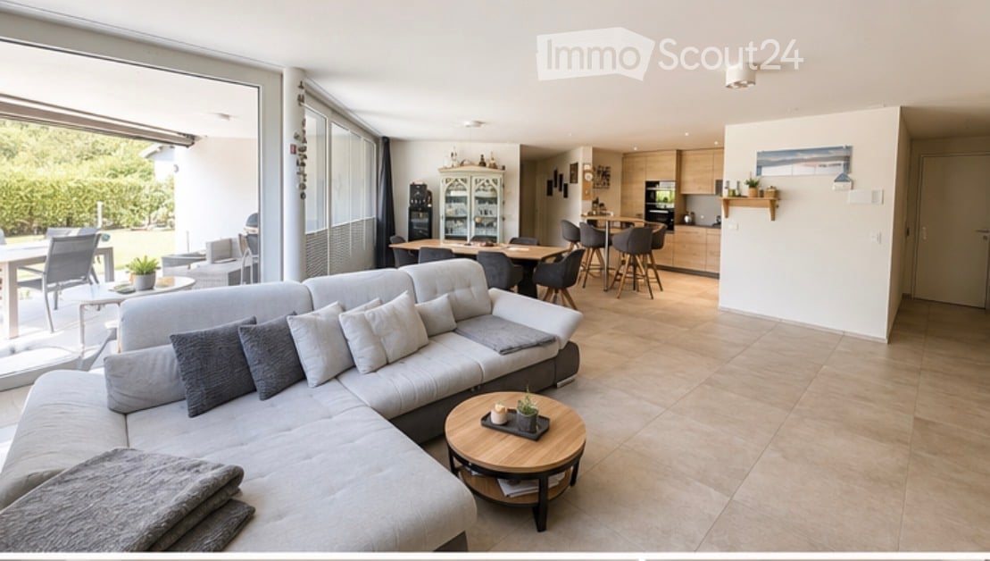 Open-plan living and dining area with a grey sectional sofa, coffee table, dining table with chairs, and a modern kitchen with cabinets and a kitchen island.