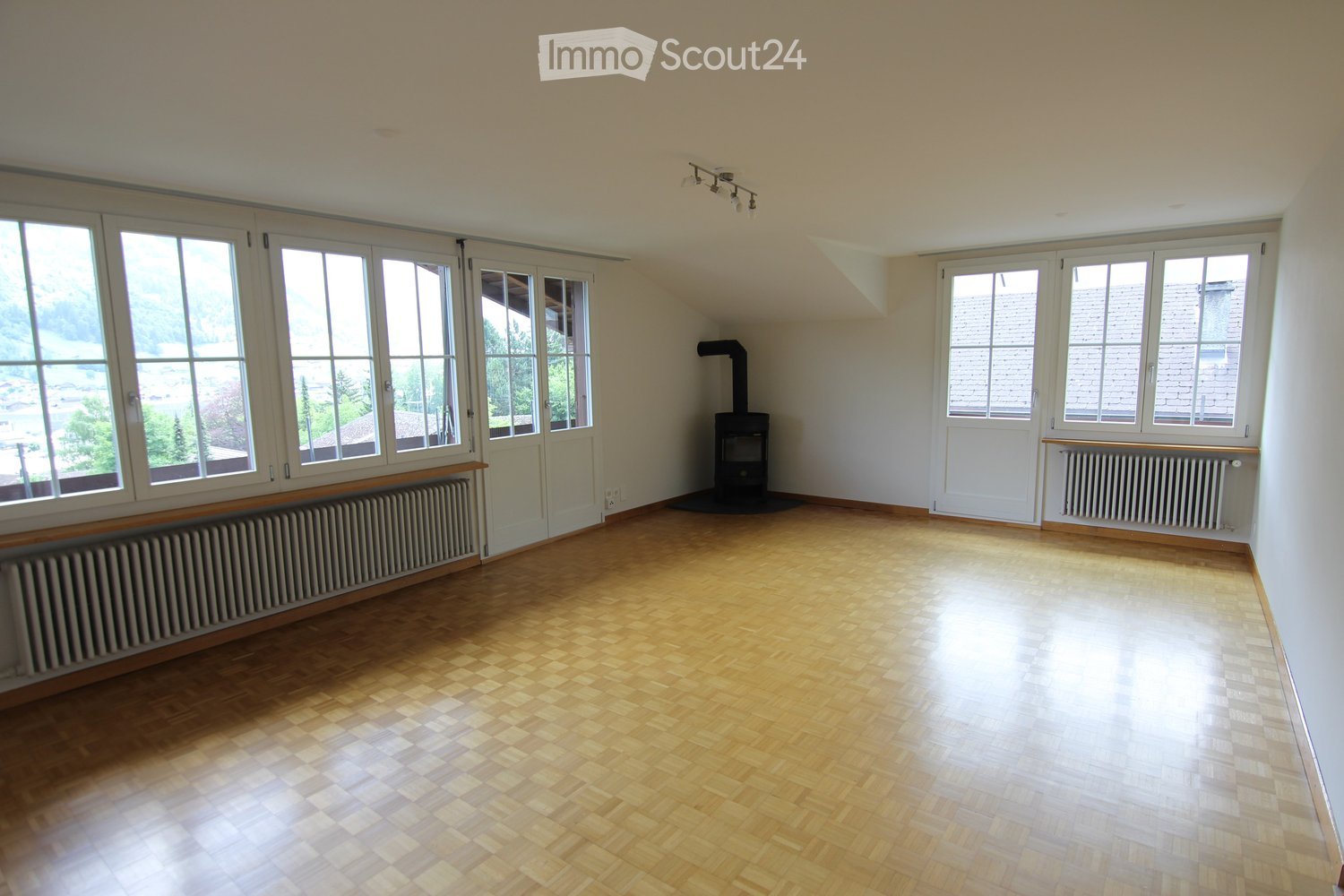 Empty room with wooden flooring, large windows, radiators, and a fireplace. No furniture or equipment present.