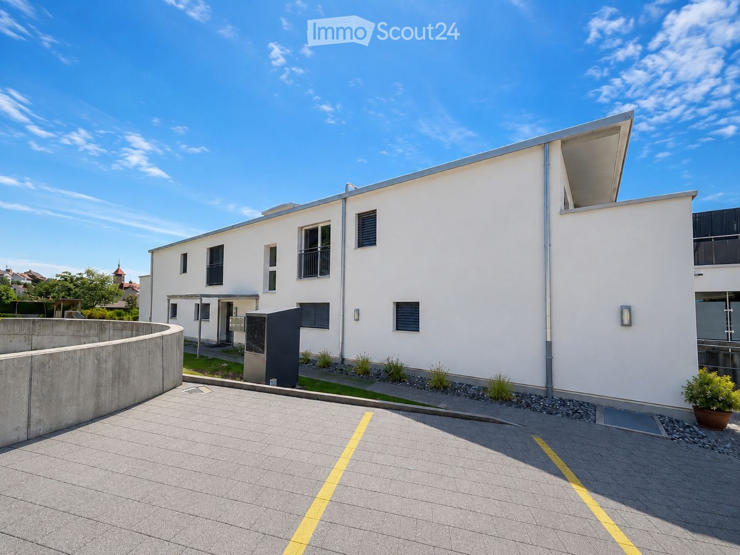 Modern two-story white building with large windows, a raised ground floor, and a small garden area.