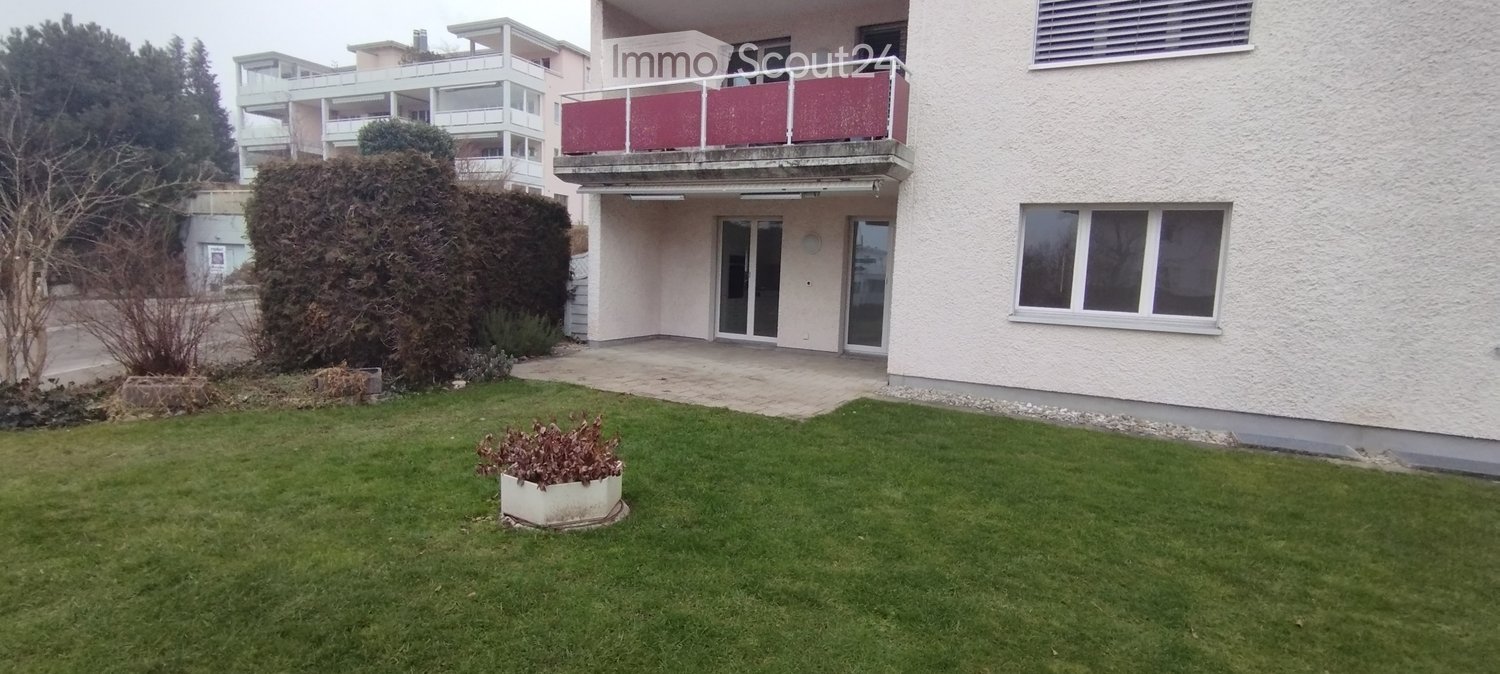 Modern multi-story residential building with balconies, large windows, and a well-maintained lawn in front.