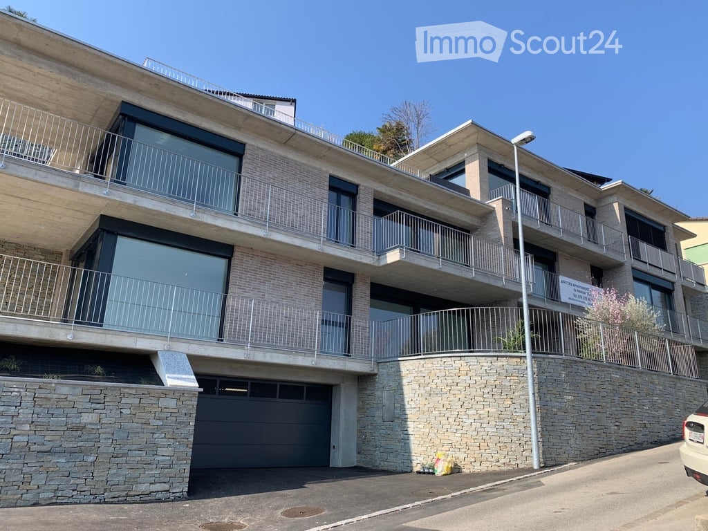 Modern multi-story building with balconies, large windows, and a stone facade. Features include a garage and a raised ground floor.