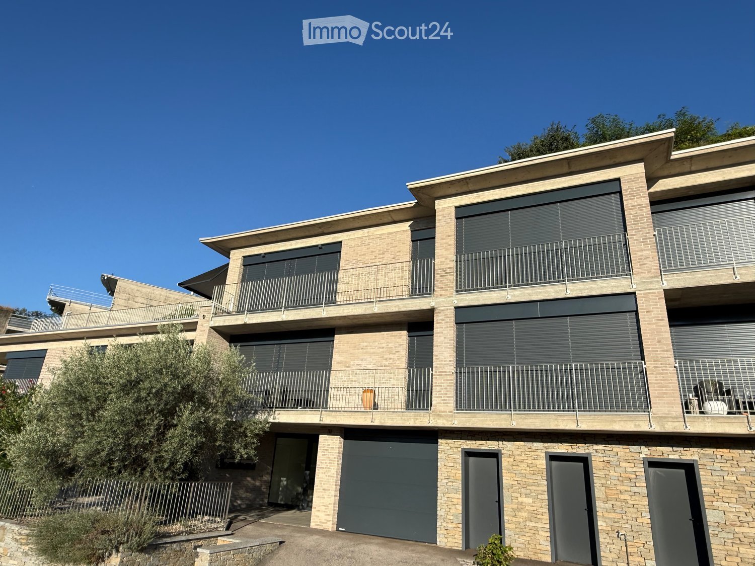 Modern two-story brick building with multiple balconies, large windows, and a garage entrance.
