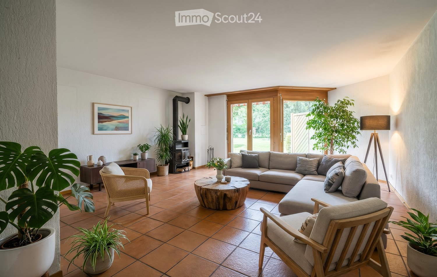 Modern living room with a grey sectional sofa, wooden coffee table, wicker chairs, fireplace, and several potted plants.