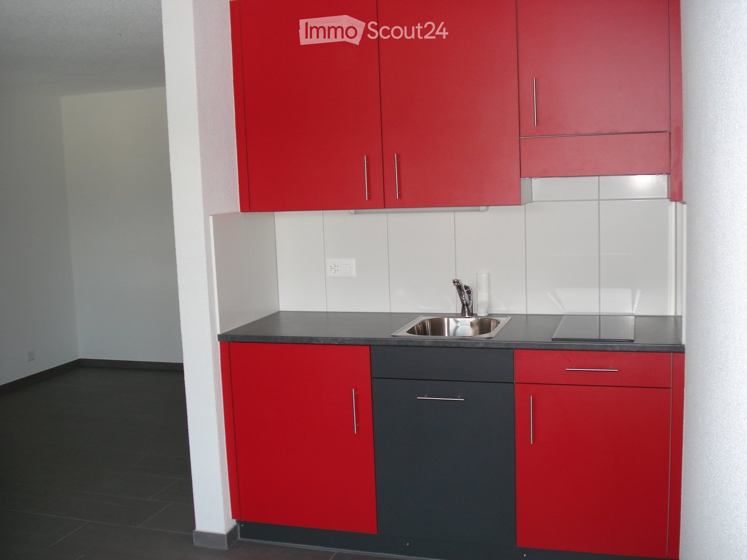 Modern kitchen with red and grey cabinets, a stainless steel sink, and a sleek countertop.