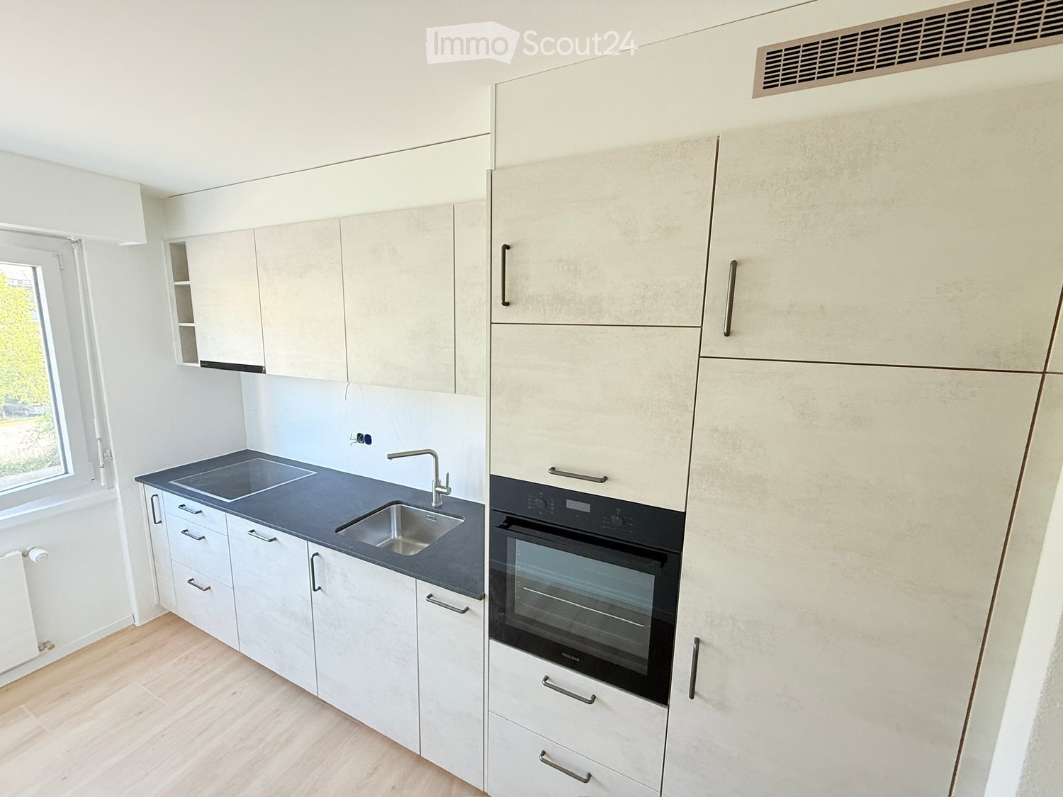 Modern kitchen with white cabinets, dark countertop, sink, faucet, and built-in oven.