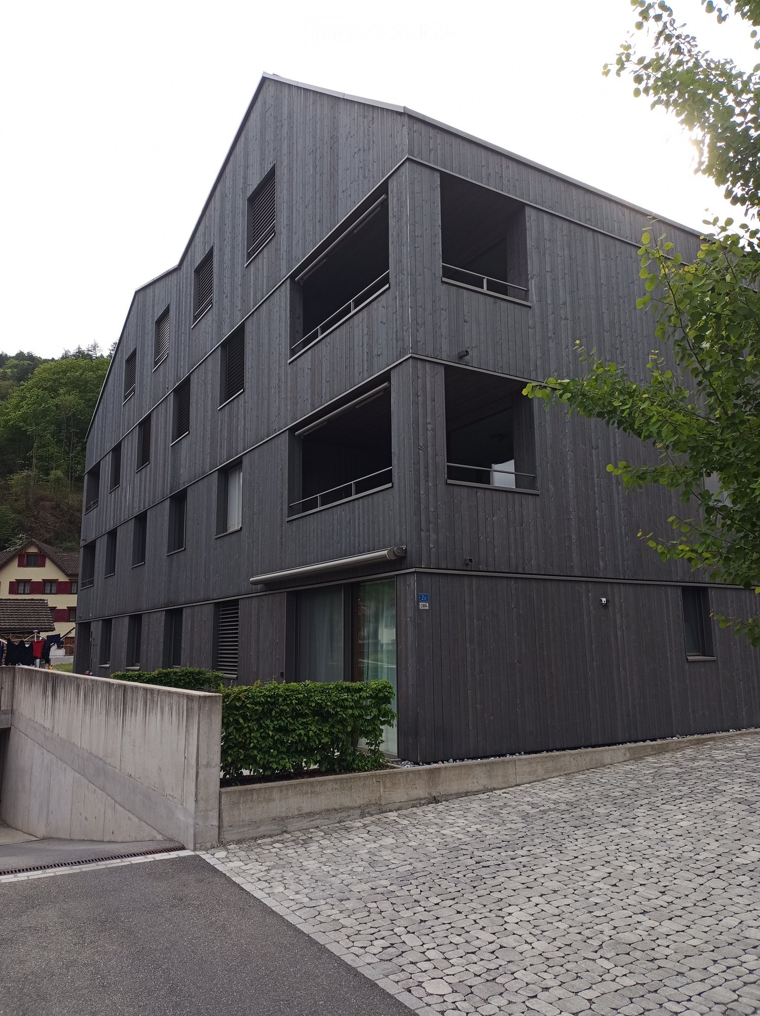 Modern, multi-story building with dark wooden facade, large windows, and a raised ground floor entrance.