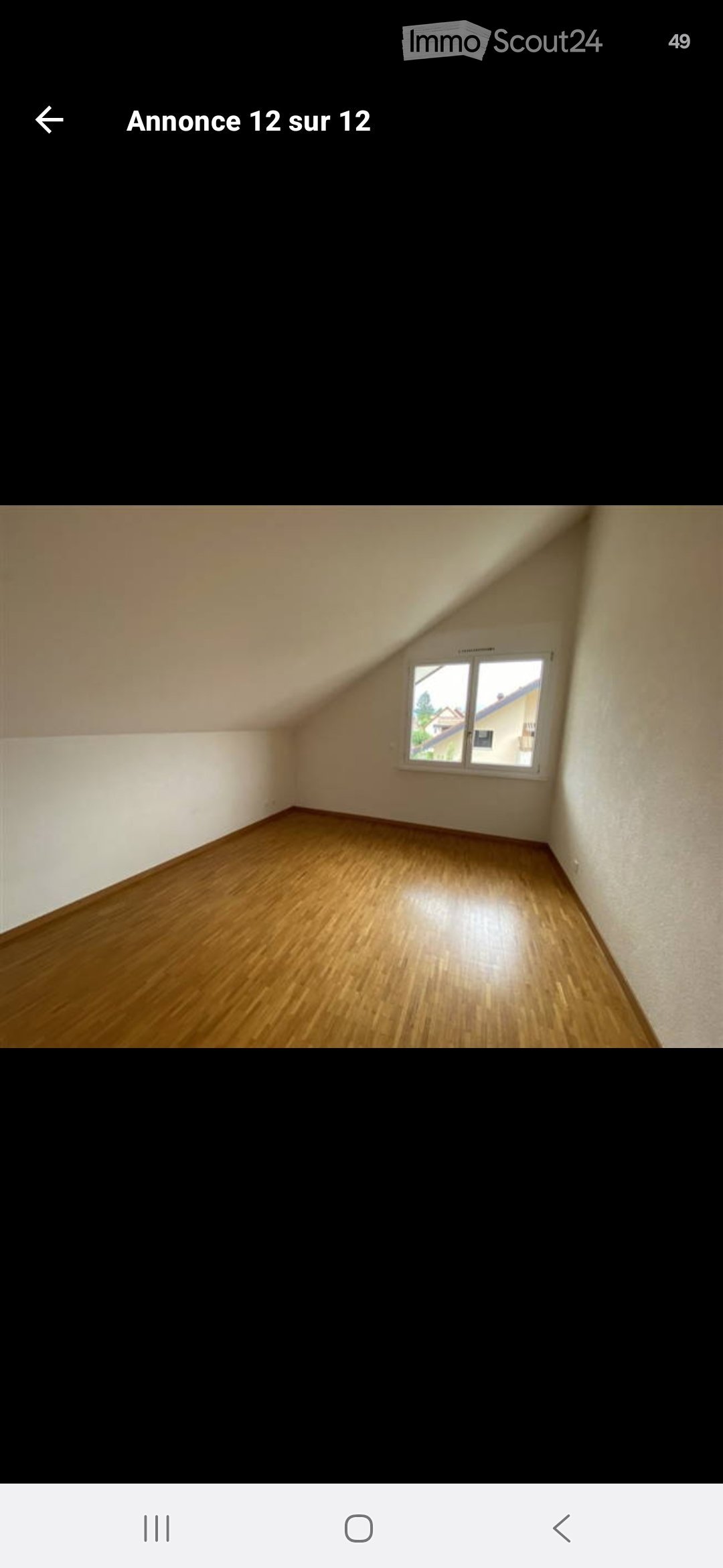 Empty room with wooden flooring and white walls, featuring a single window with a view of neighboring buildings.
