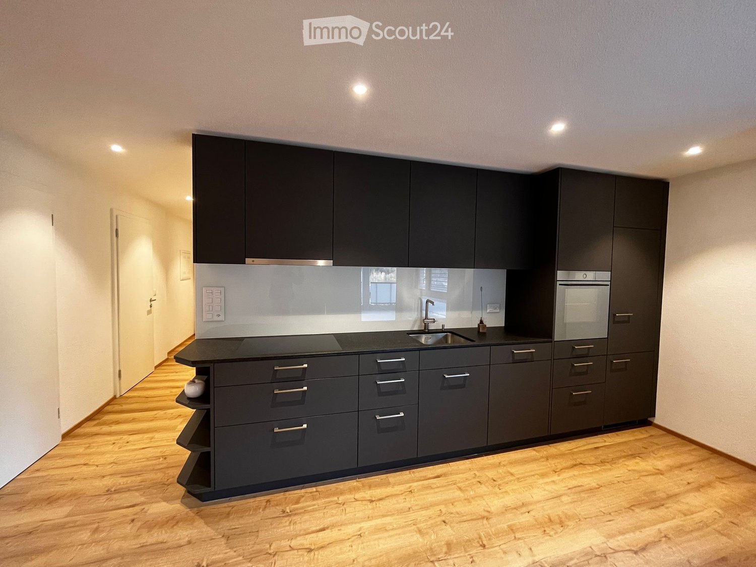 modern kitchen with black cabinets, wooden floor, black countertop, sink, faucet, integrated oven