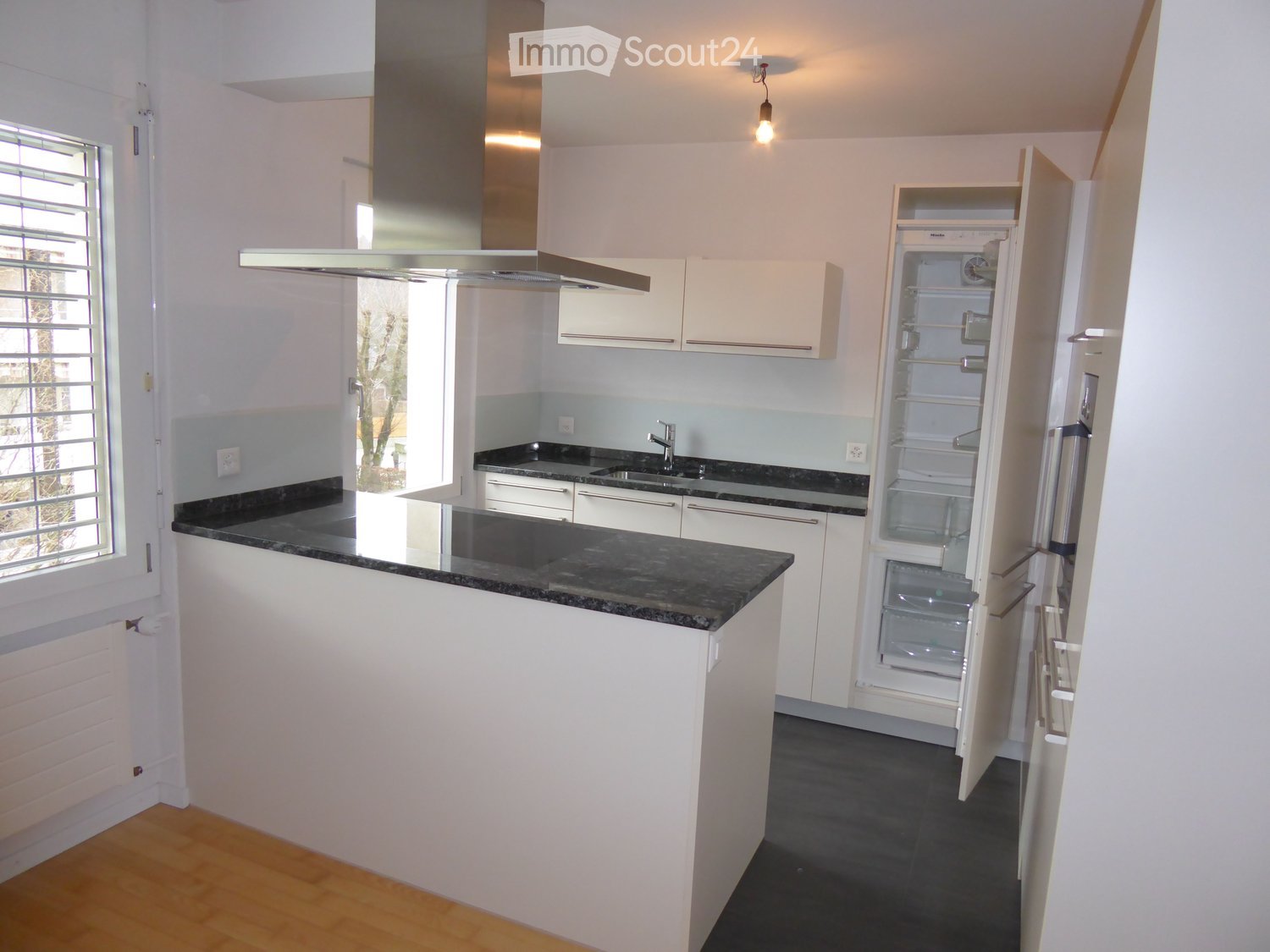 modern kitchen with island, granite countertops, stainless steel appliances, white cabinets, open refrigerator, sink with faucet, exhaust hood, wooden floor