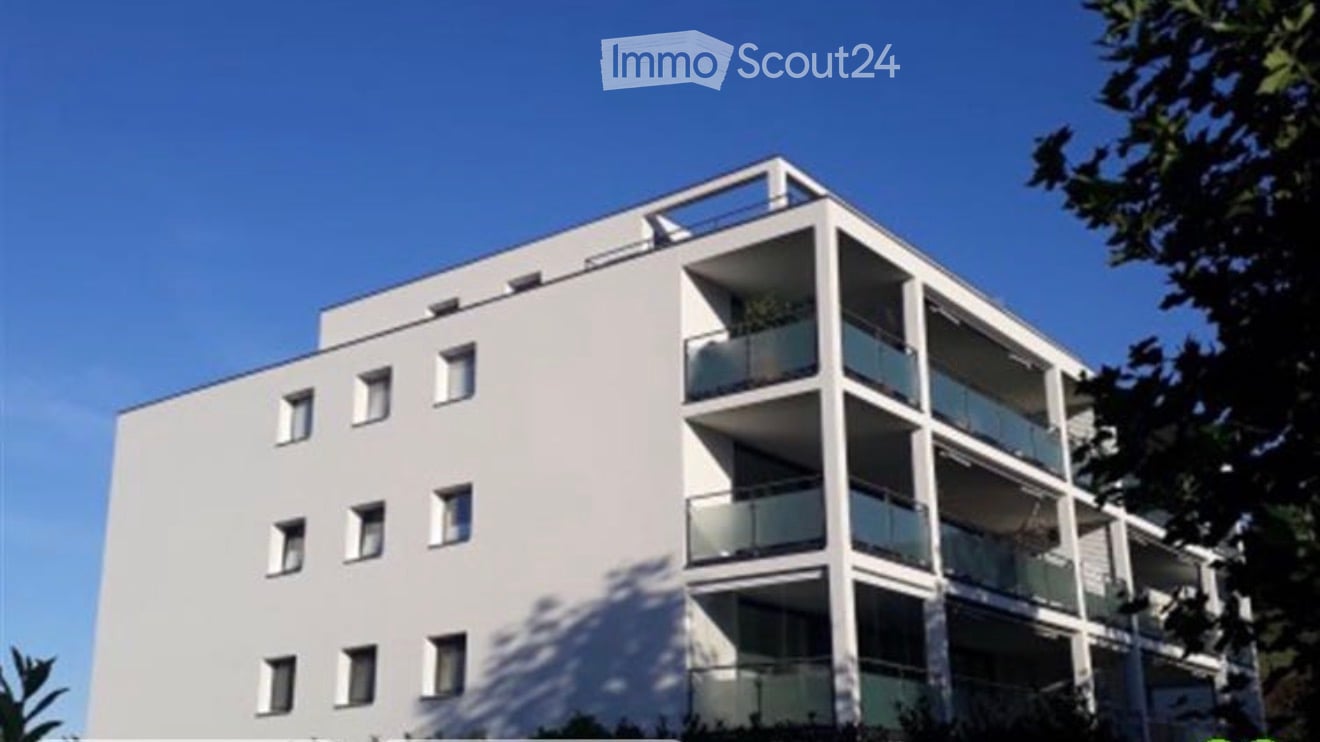 Modern multi-story apartment building with white facade, multiple balconies, and large windows.