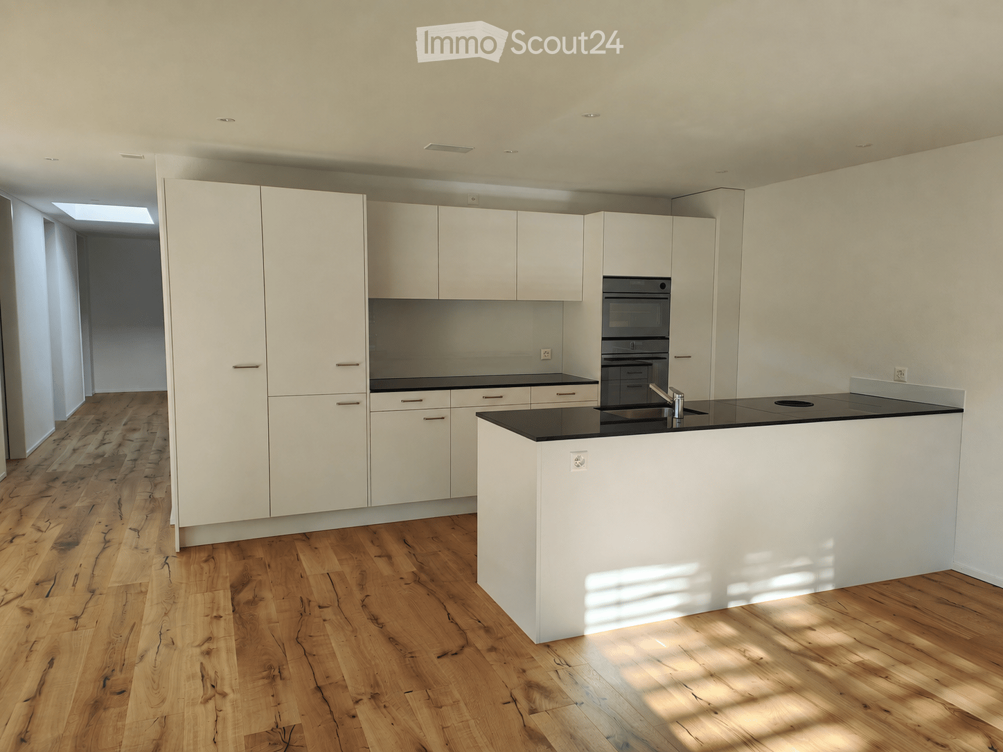 Modern kitchen with white cabinets, black countertops, and a central island. Features a wooden floor and built-in appliances.