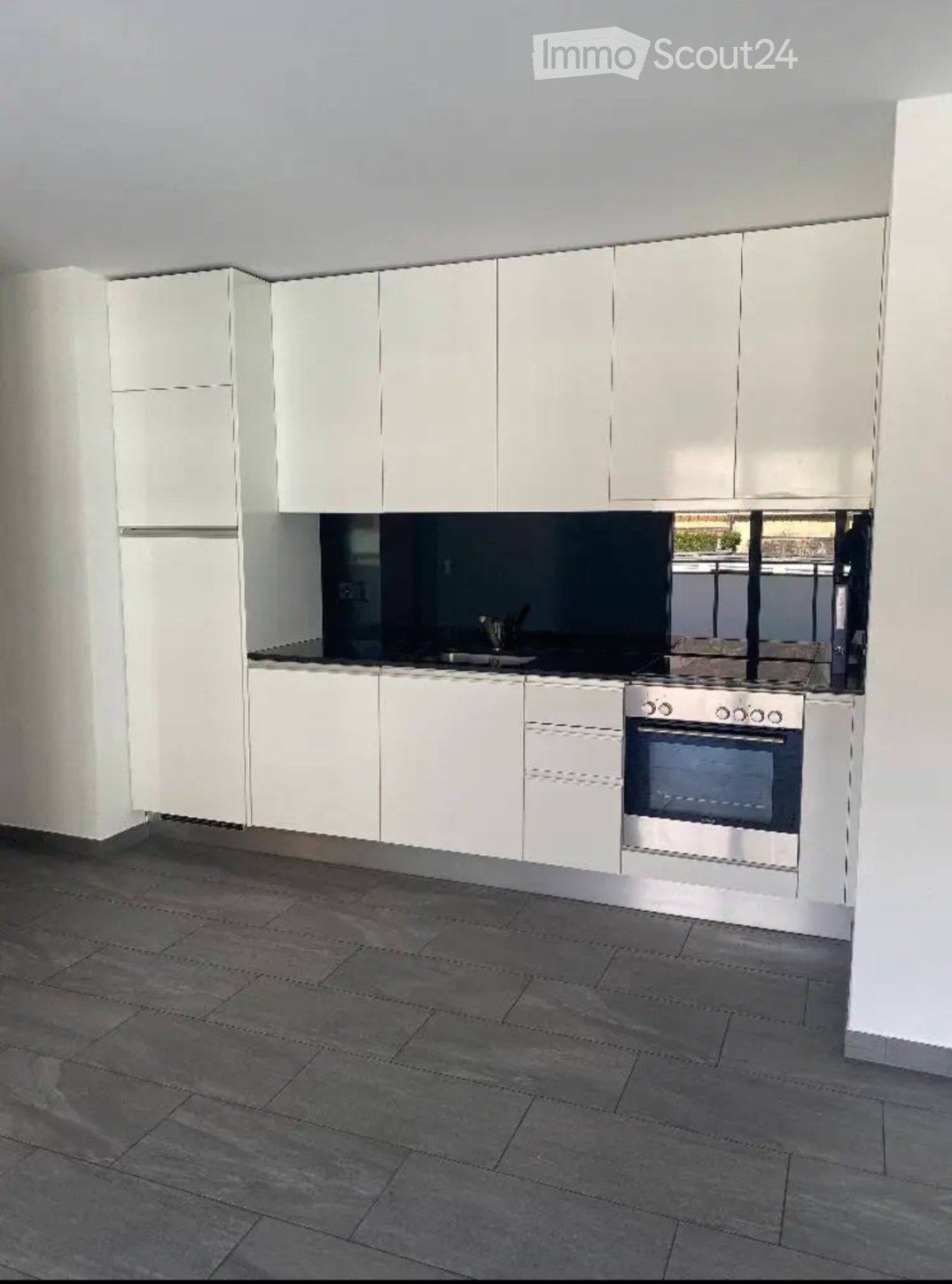 Modern kitchen with white cabinets, stainless steel oven, and dark tiled floor.