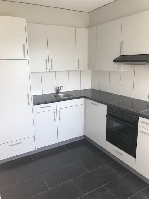 Modern kitchen with white cabinets, black countertops, and black tiled flooring. Features a sink, oven, and built-in cabinets.
