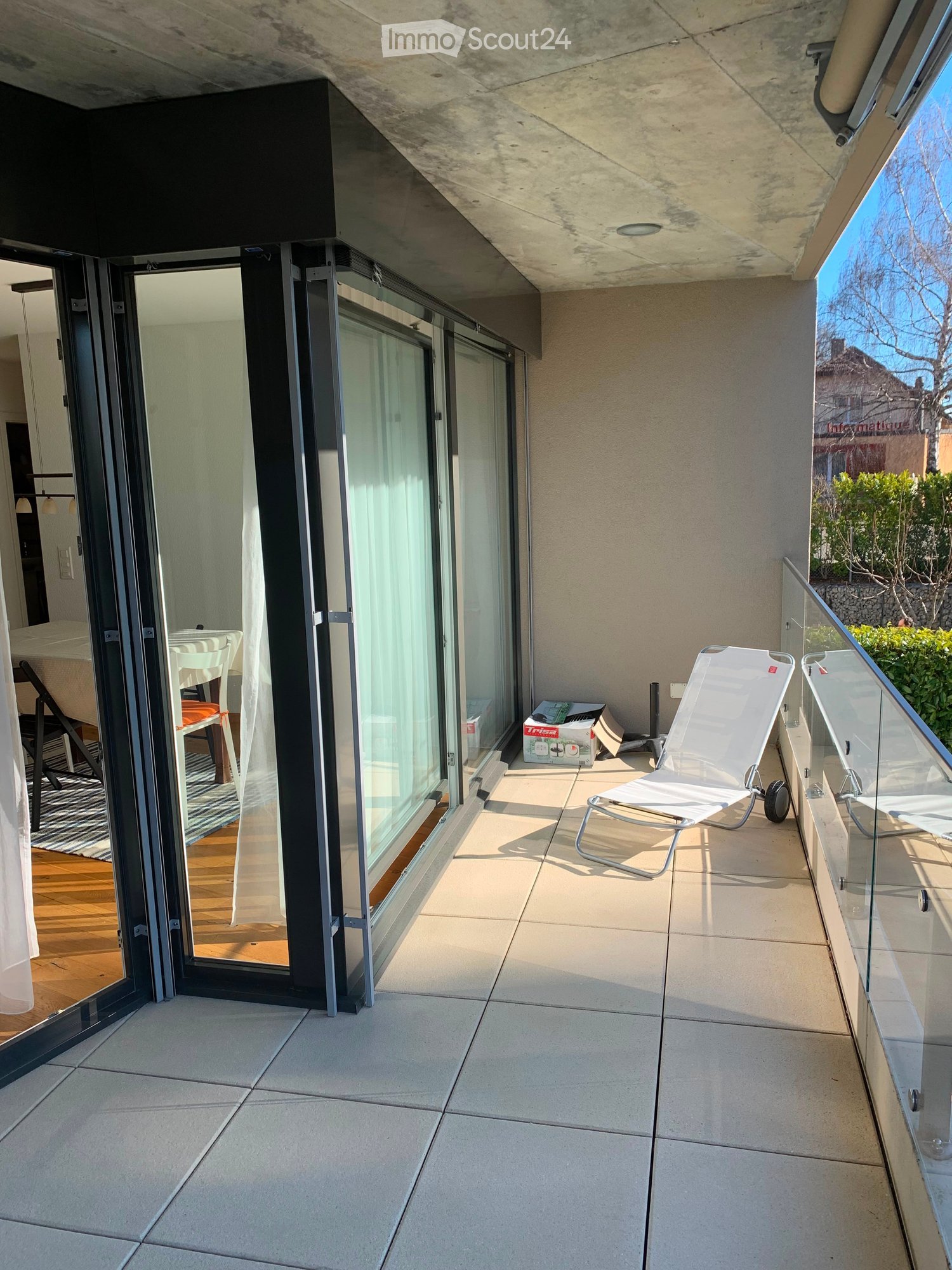 Balcony with tiled floor, glass railing, and a white lounge chair.