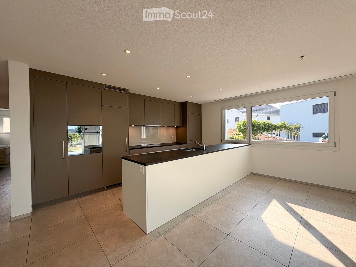 Modern kitchen with grey cabinetry, white island, black countertop, and stainless steel sink.