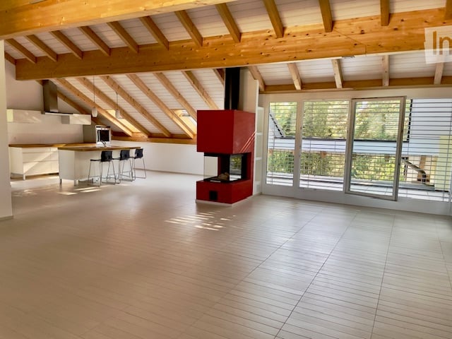 Open-plan living and kitchen area with exposed wooden beams, a modern fireplace, and large sliding glass doors leading to a balcony.